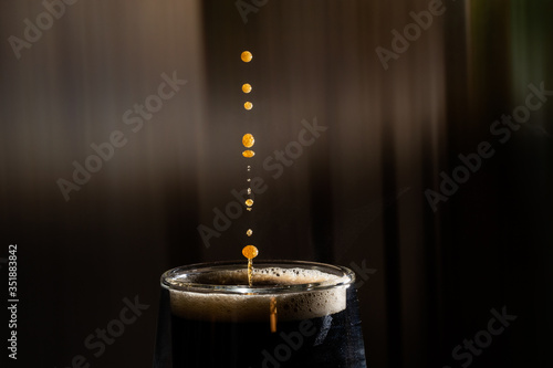 Coffee splash. Reaction of a falling drop on the hot, steaming and frothy coffee surface in a modern glass transparent cup. Studio photo with matching colored background