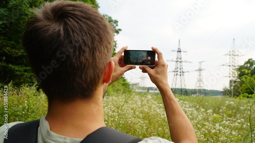 Adult man taking a picture with smart phone. Outdoor shot in nature. Shallow depth of field. Back view