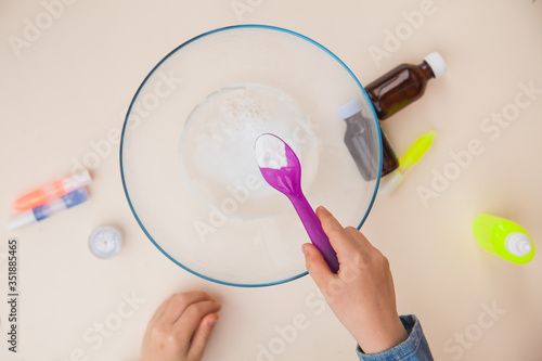 Making slime, step by step instruction, step two, adding soda. Child's hands preparing homemade toy. photo