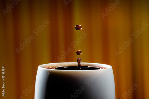 Red wine splash. Reaction of a falling drop on a red wine  surface in a completely filled white plastic cup. Studio photo with matching orange striped colored background. Beautiful wine drop.