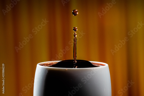 Red wine splash. Reaction of a falling drop on a red wine  surface in a completely filled white plastic cup. Studio photo with matching orange striped colored background. Beautiful wine drop.