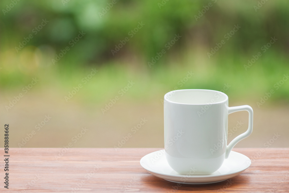 White porcelain cup on wooden table, blurred nature background White porcelain cup on wooden table, blurred nature background