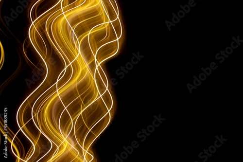 Long exposure photograph of neon gold colour in an abstract swirl, parallel lines pattern against a black background. Light painting photography.