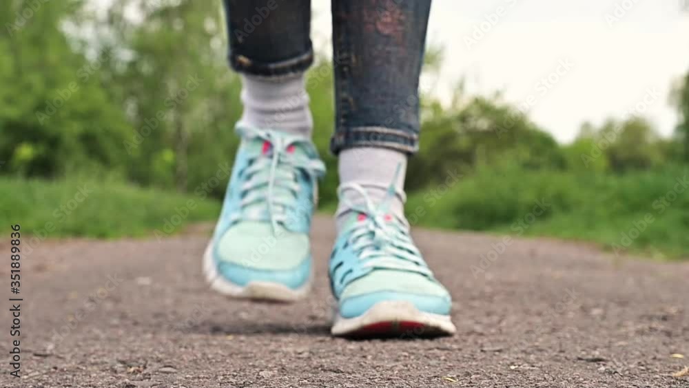 woman in sneakers walks on a dirt road. Girl dressed in jeans and sneakers is walking through the park. Closeup legs, one girl walking woman in sneakers walks on a dirt road. Girl dressed in jeans and sneakers is walking through the park. Closeup legs, one girl walking