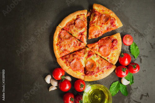 Top view of hot pepperoni pizza,Tasty pepperoni pizza and cooking ingredients tomatoes basil on black background.