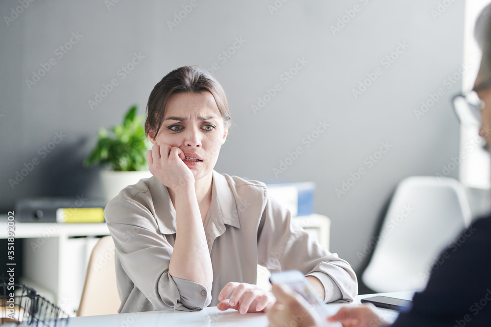 Young nervous female applicant looking at her resume held by employer Young nervous female applicant looking at her resume held by employer
