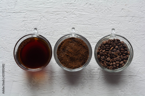 Three cups of ground coffee, coffee beans and brewed coffee in one row