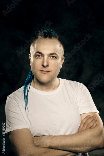 Portrait of a young man with an unusual hairstyle of mohawk from blue braids in sportswear posing full face on a gray