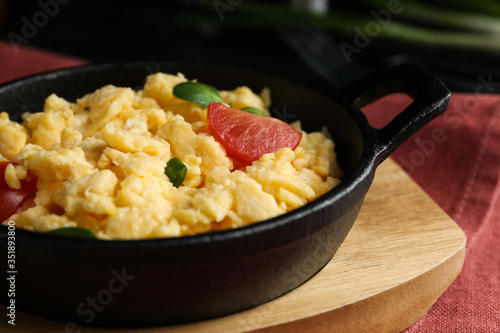 Tasty scrambled eggs with sprouts and cherry tomato in frying pan on table, closeup