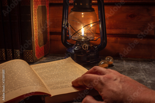 Reading a book in the light of an old hand-held kerosene lamp glows softly in a dark room on the table. Vintage style. The light in the darkness. Atmospheric photo in the loft style.