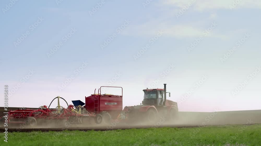 A sowing tractor with a seeder trailer drives through a dug-up field. Tractor drives through the field sowing seeds A sowing tractor with a seeder trailer drives through a dug-up field. Tractor drives through the field sowing seeds