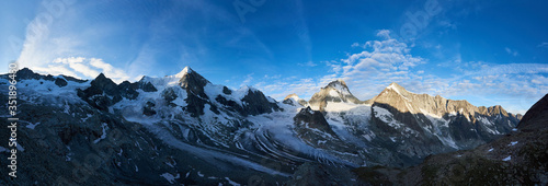 Panoramic shot of new day in the Swiss Alps, morning bright sun is shining at the ridge of rocky mountains, while the valley is still in the shadow
