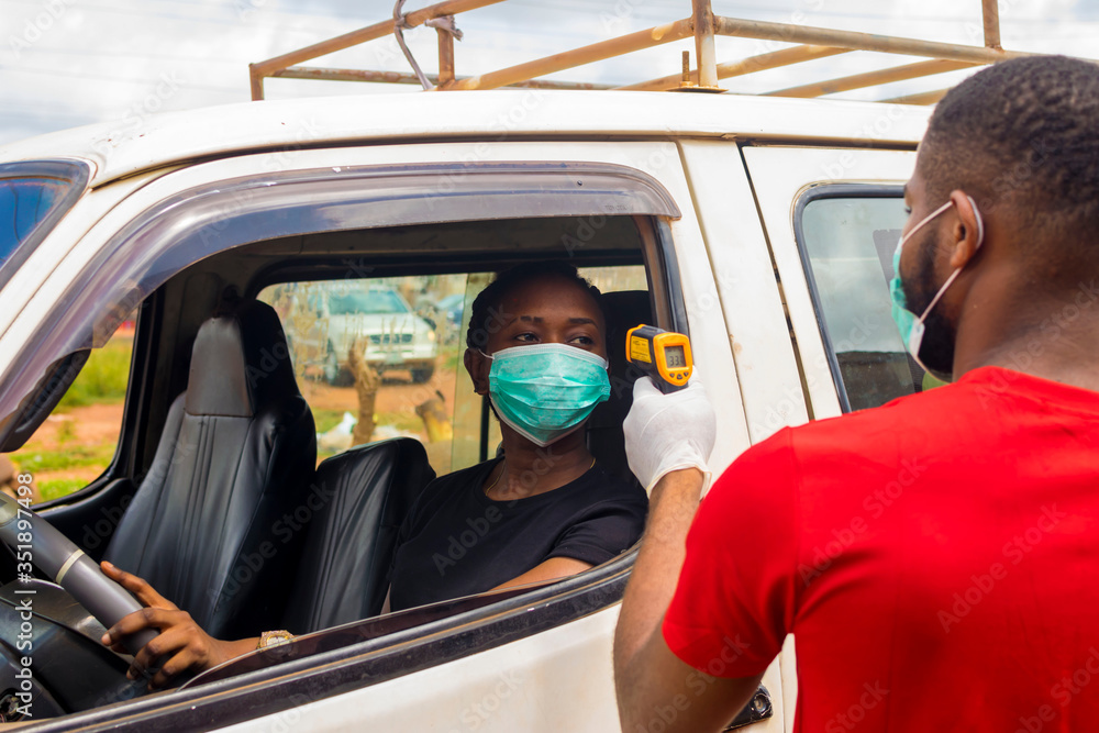 Naklejka premium young black man wearing a nose mask, checking the temperature of a black woman driving a car