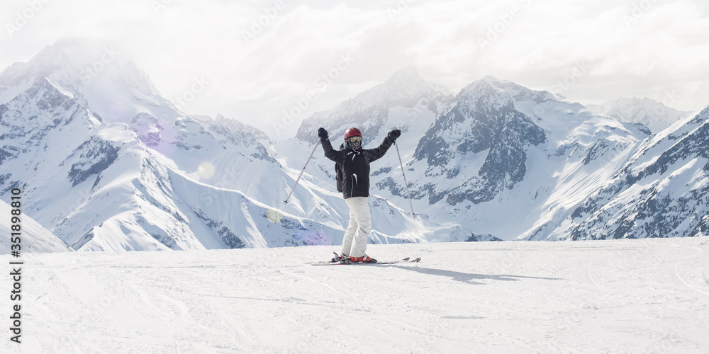 Happy and positive female skier on the top of the mountain raise up hand with enjoy and happiness and enjoy in beautiful snowy alps mountain range. Winter season sport and recreation travel concept