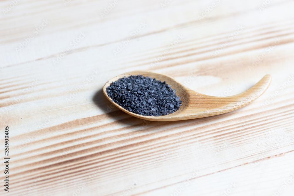 Black (burned with powder) salt in spoon on wooden background Black (burned with powder) salt in spoon on wooden background