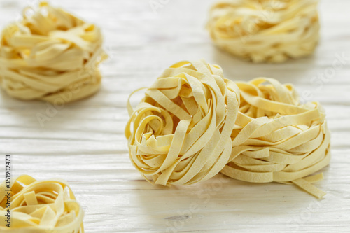 Tagliatelle. Traditional Italian homemade raw pasta on a white wooden background close up. Nests. Selective focus
