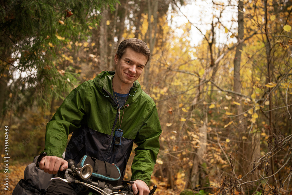 Smiling handsome man in green windbreaker on bicycle in autumn forest