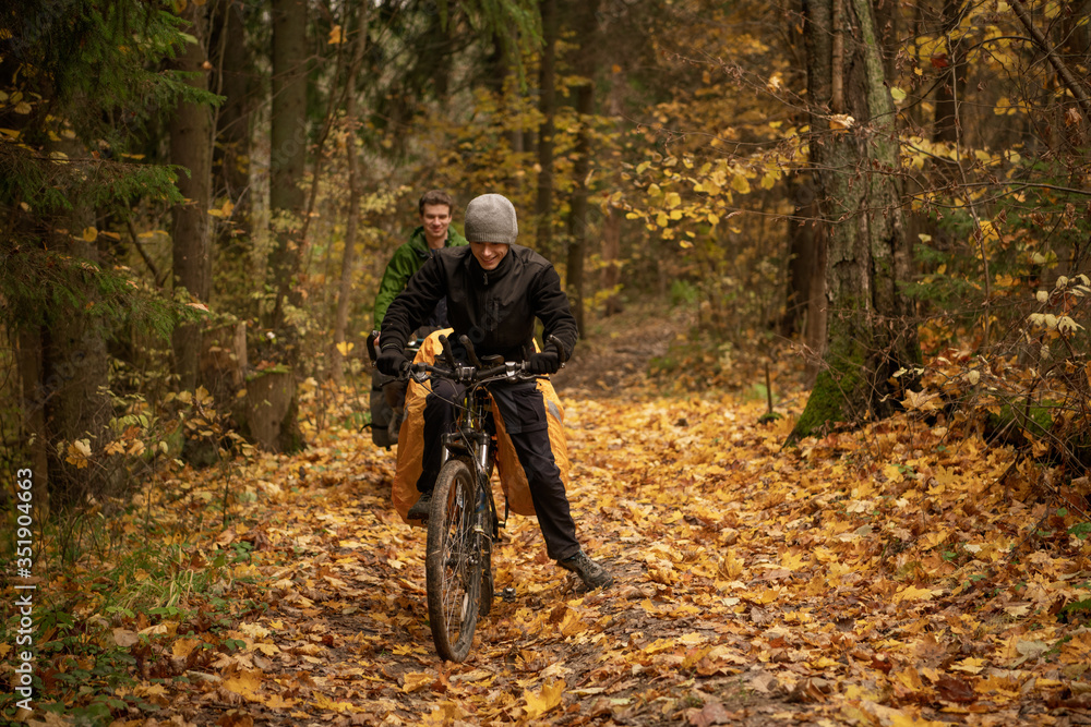 Smiling handsome man in black windbreaker on bicycle in autumn forest