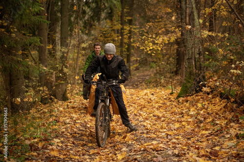 Smiling handsome man in black windbreaker on bicycle in autumn forest