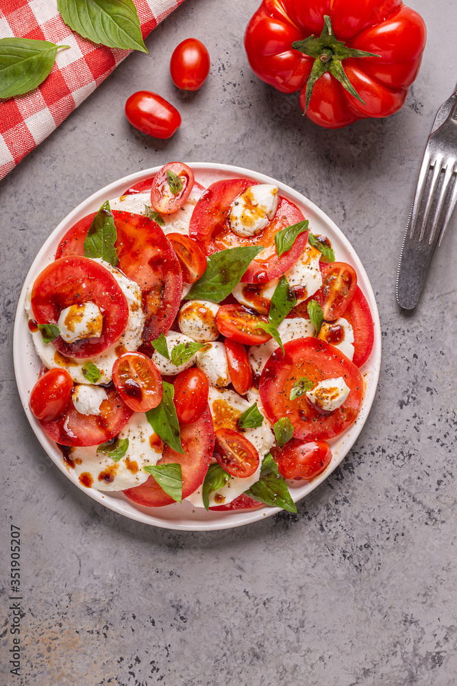 Italian caprese salad with sliced tomatoes, mozzarella cheese, basil, olive oil, balsamic vinegar.