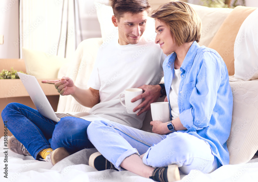 Couple moving in together relaxing on sofa couch with laptop tablet computer and boxes Couple moving in together relaxing on sofa couch with laptop tablet computer and boxes