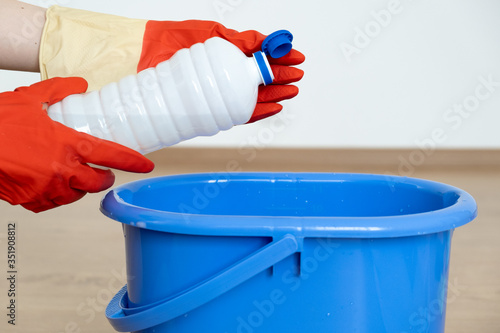  Hands in gloves for cleaning pour a cleaner for cleaning surfaces over a blue bucket.