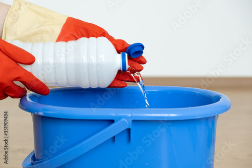  Hands in gloves for cleaning pour a cleaner for cleaning surfaces over a blue bucket.