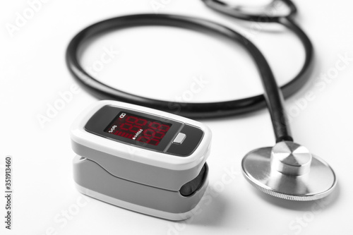 Modern fingertip pulse oximeter and stethoscope on white background, closeup