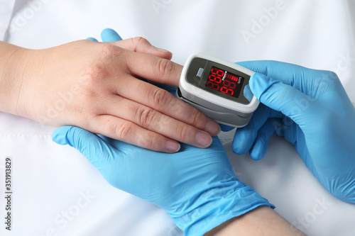 Doctor examining patient with modern fingertip pulse oximeter in bed, closeup photo