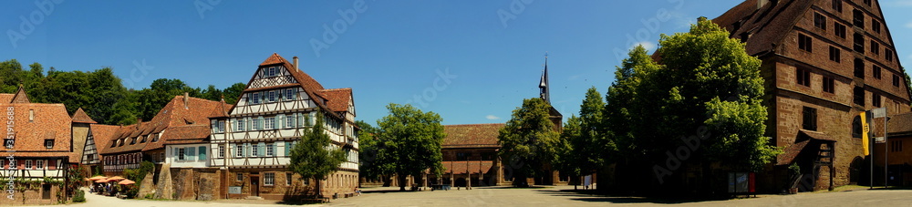 weites Panorama von Klosterkirche in Maulbronn mit Klosterhof und alten Gebäuden unter blauem Himmel weites Panorama von Klosterkirche in Maulbronn mit Klosterhof und alten Gebäuden unter blauem Himmel