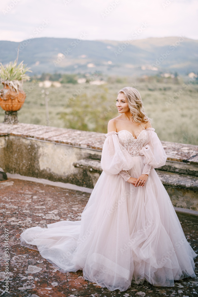 Wedding at an old winery villa in Tuscany, Italy. The bride in a white magnificent dress, with bare shoulders and magnificent sleeves, walks on the roof of an old villa.