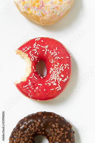 Donut day. Bitten colored donuts with colorful sprinkles on white background. Copy space, close-up