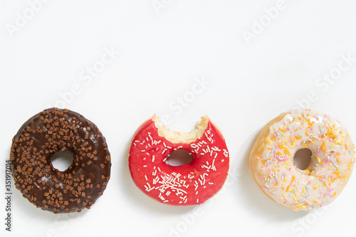 Donut day. Bitten colored donuts with colorful sprinkles on white background. Copy space, close-up