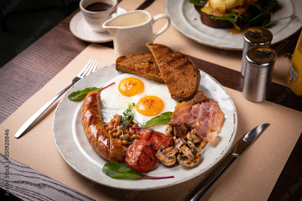 Full English breakfast - fried egg, baked beans, bacon, sausages on a dark rusty background, toasts. Full English breakfast - fried egg, baked beans, bacon, sausages on a dark rusty background, toasts.