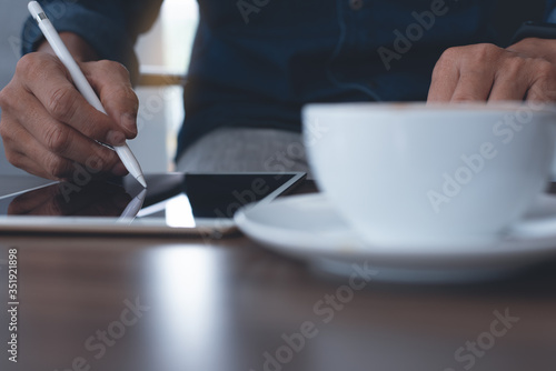 Man graphic designer using stylus pen on digital tablet computer on table for working at coffee shop coworking space