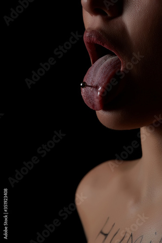 female tongue with piercing on a black background. the girl stuck out her pierced tongue