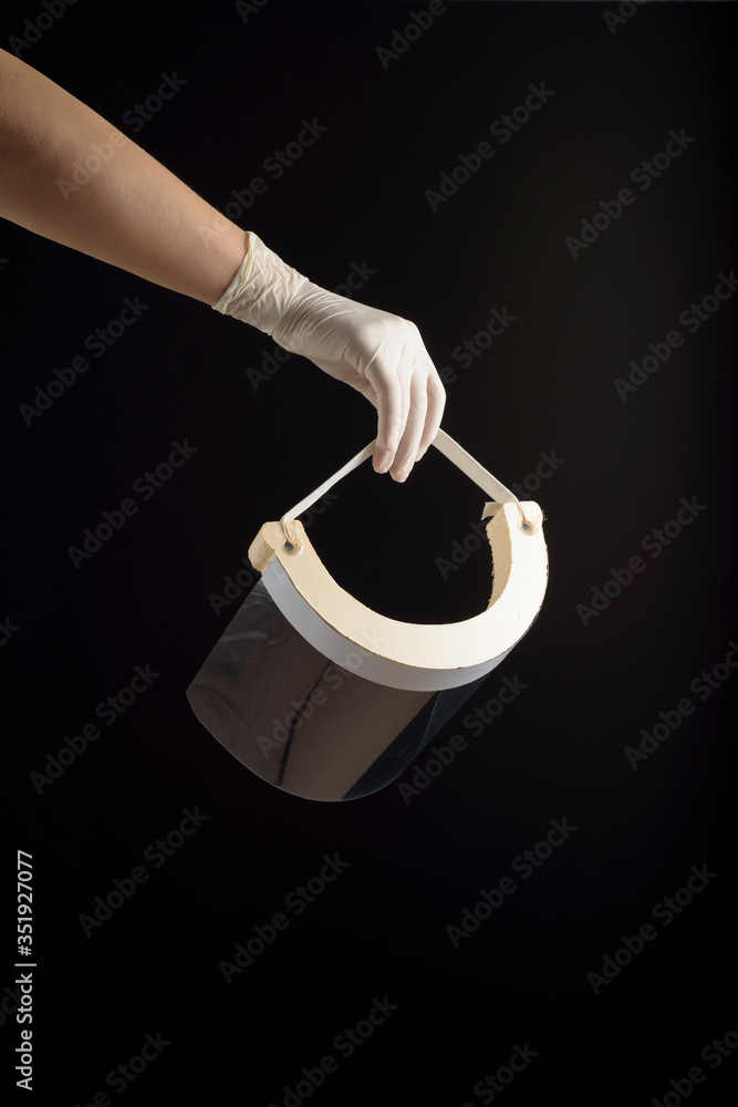 Hand with latex glove holding a face screen, on black background. Protection for contagions. Hand with latex glove holding a face screen, on black background. Protection for contagions.