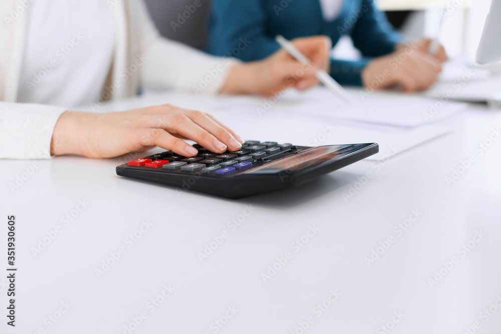 Accountant checking financial statement or counting by calculator income for tax form, hands closeup. Business woman sitting and working with colleague at the desk in office toned in blue. Tax and Accountant checking financial statement or counting by calculator income for tax form, hands closeup. Business woman sitting and working with colleague at the desk in office toned in blue. Tax and