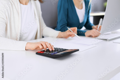 Accountant checking financial statement or counting by calculator income for tax form  hands closeup. Business woman sitting and working with colleague at the desk in office toned in blue. Tax and