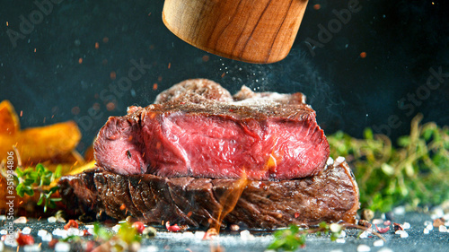 Close-up of tasty beef steak on black stone table, fire flames in foreground