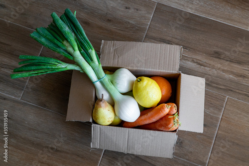 Fresh vegetables in cardboard box on brown wood background.