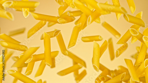 flying uncooked italian pasta penne on gold background, freeze motion.