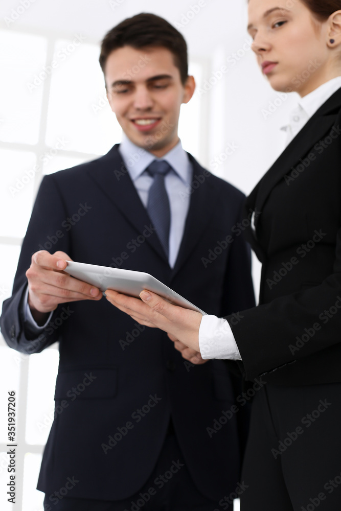 Businessman and woman using tablet computer for discussing questions in office. Partners or colleagues at meeting. Business cooperation concept