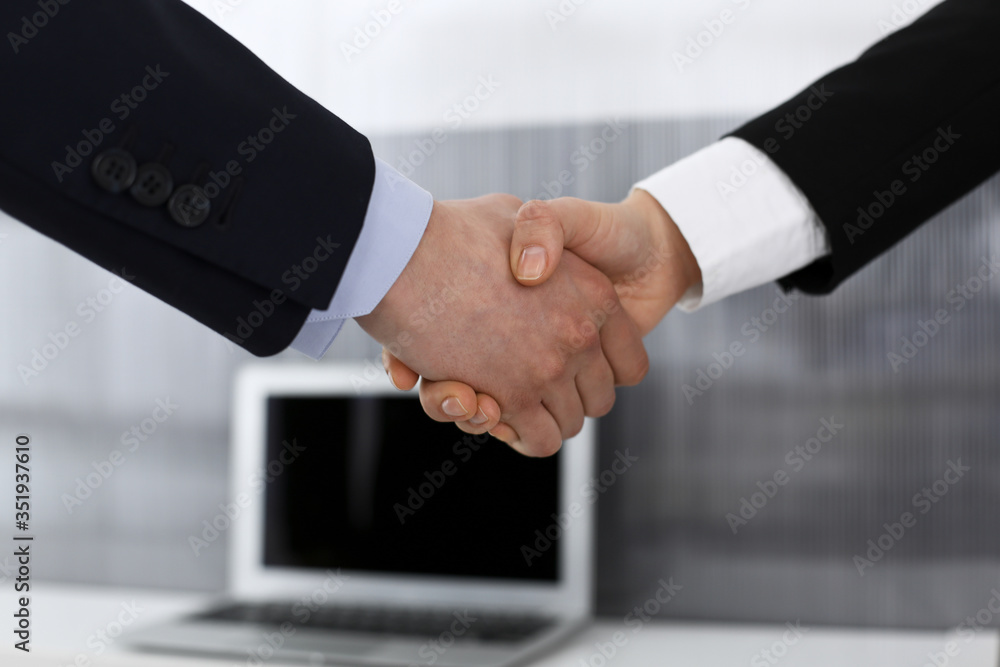 Businessman and woman shaking hands in office. Concept of handshake as success symbol in business Businessman and woman shaking hands in office. Concept of handshake as success symbol in business