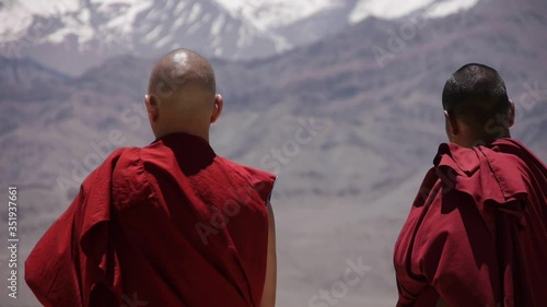 Two Buddhist monks look into the distance at the high snow peaks of the Himalayas