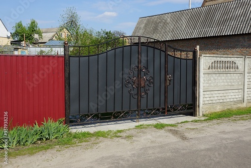 gray iron gate with black forged pattern and red fence on the street