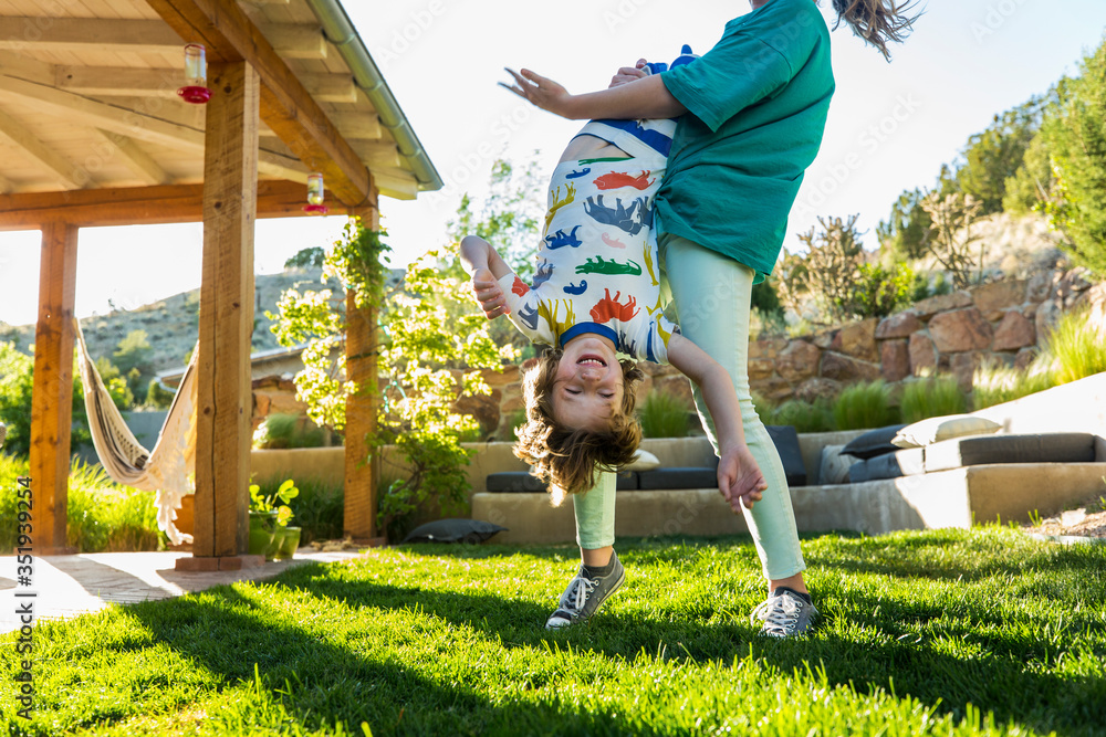 © Marc Romanelli - teenager sister holding her younger brother upside down on green lawn at sunset © Marc Romanelli - teenager sister holding her younger brother upside down on green lawn at sunset
