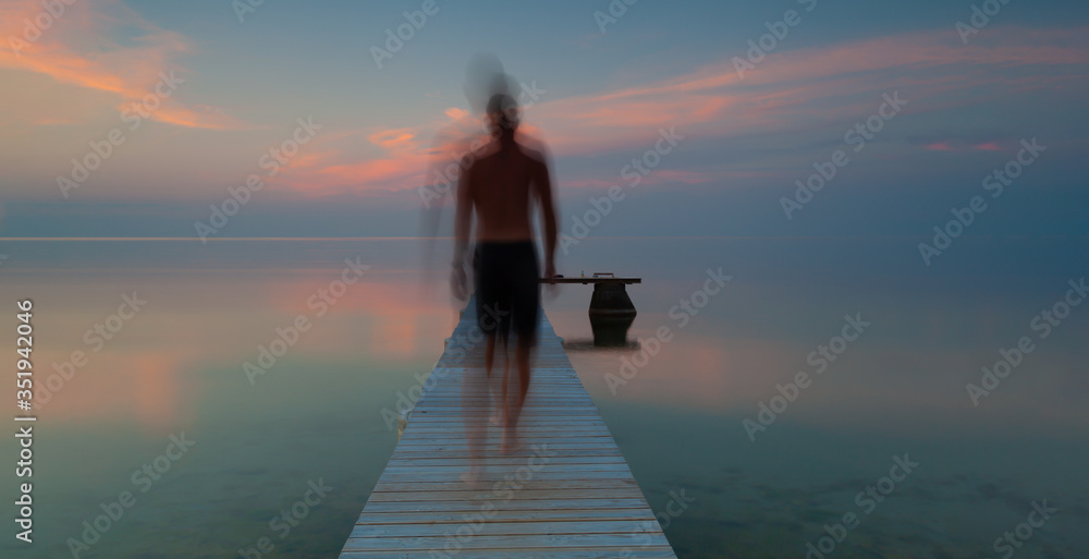 Long Exposure, a blurred person goes out on a jetty in the summer night on Gotland, Sweden. Long Exposure, a blurred person goes out on a jetty in the summer night on Gotland, Sweden.