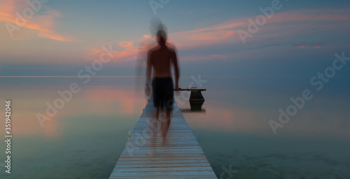 Long Exposure, a blurred person goes out on a jetty in the summer night on Gotland, Sweden. 