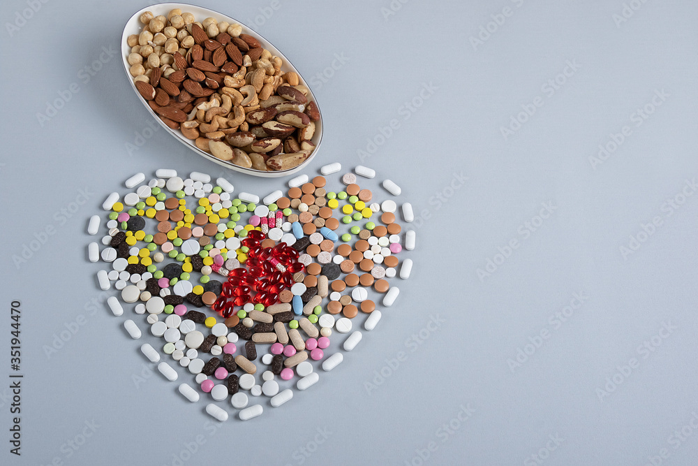 multicolored pills in shape of heart and different nuts in bowl on gray background. Concept of traditional medicine in healthy lifestyle multicolored pills in shape of heart and different nuts in bowl on gray background. Concept of traditional medicine in healthy lifestyle